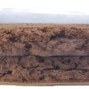 Rectangular block of compressed brown material with a rough, uneven surface texture photographed on a plain background.