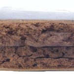 Rectangular block of compressed brown material with a rough, uneven surface texture photographed on a plain background.