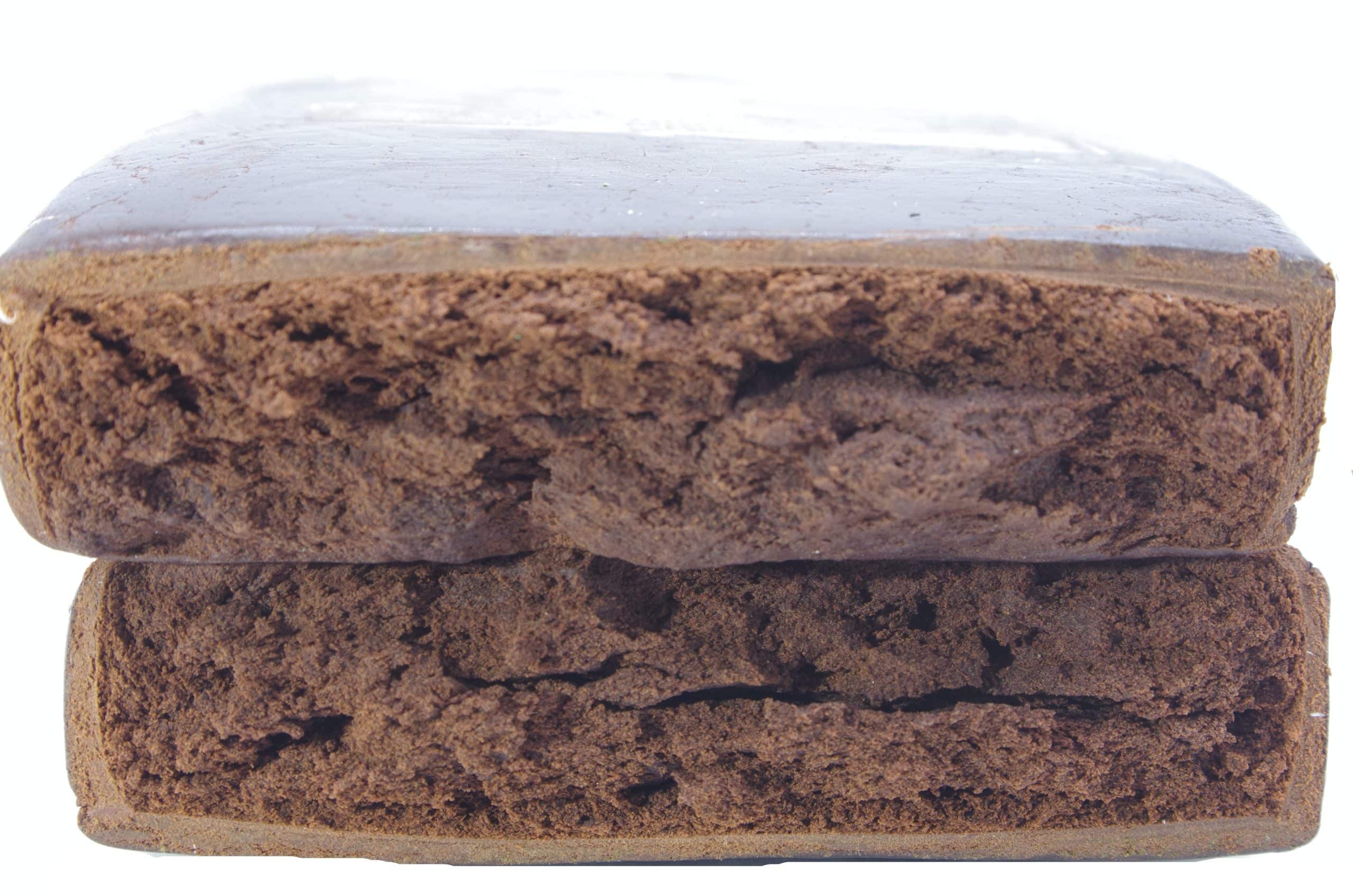 Red Lebanese Hash Rectangular block of compressed brown material with a rough, uneven surface texture photographed on a plain background.